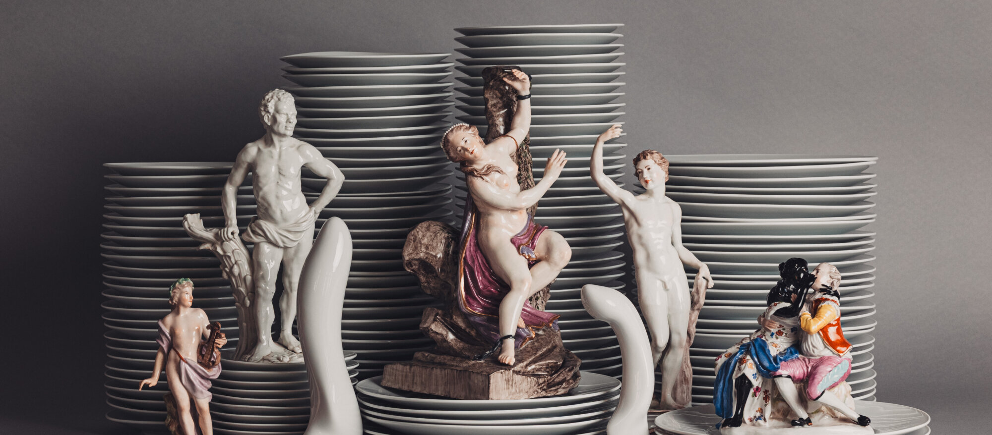 Tellerstapel, vor denen mehrere Porzellanfiguren stehen