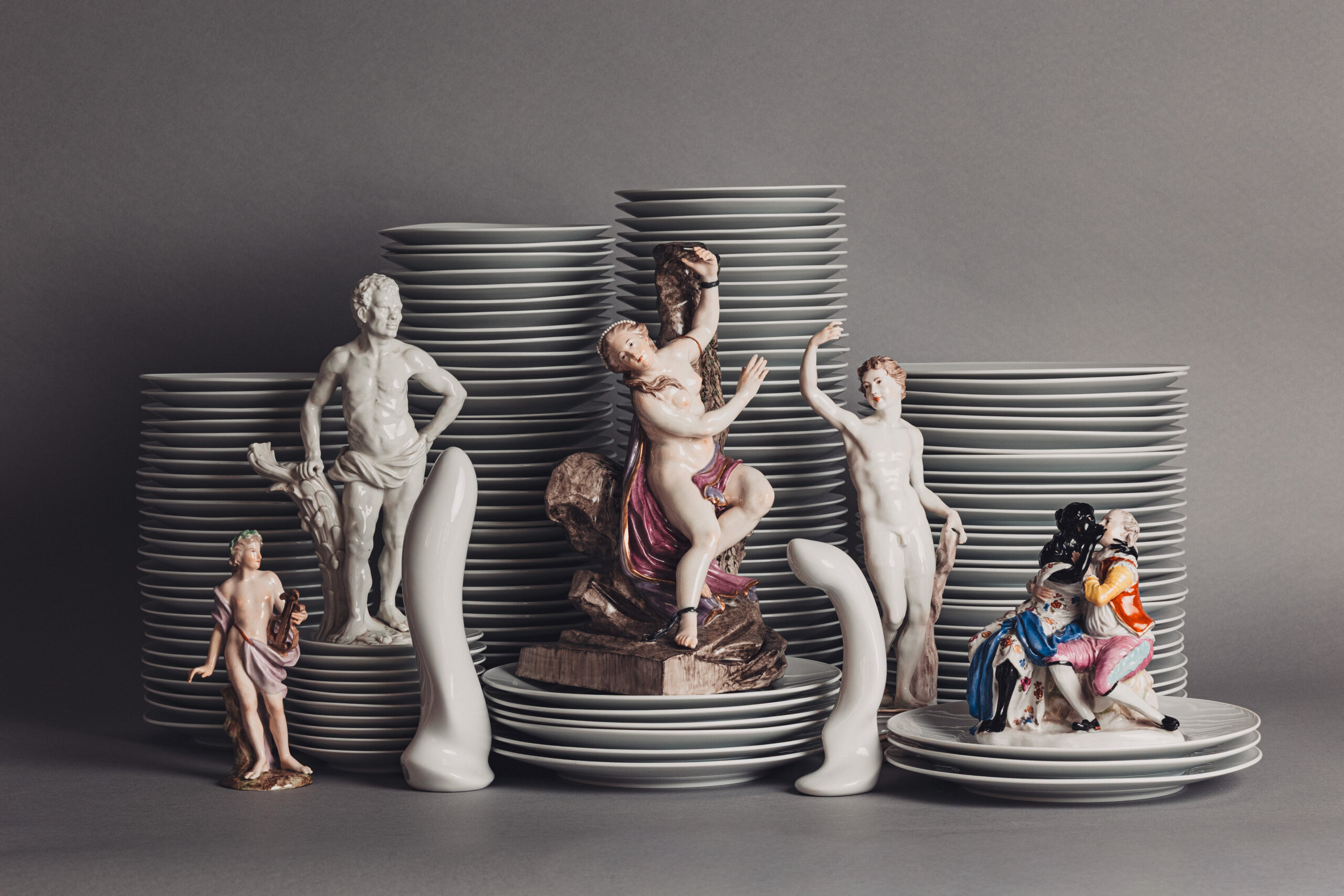 Tellerstapel, vor denen mehrere Porzellanfiguren stehen