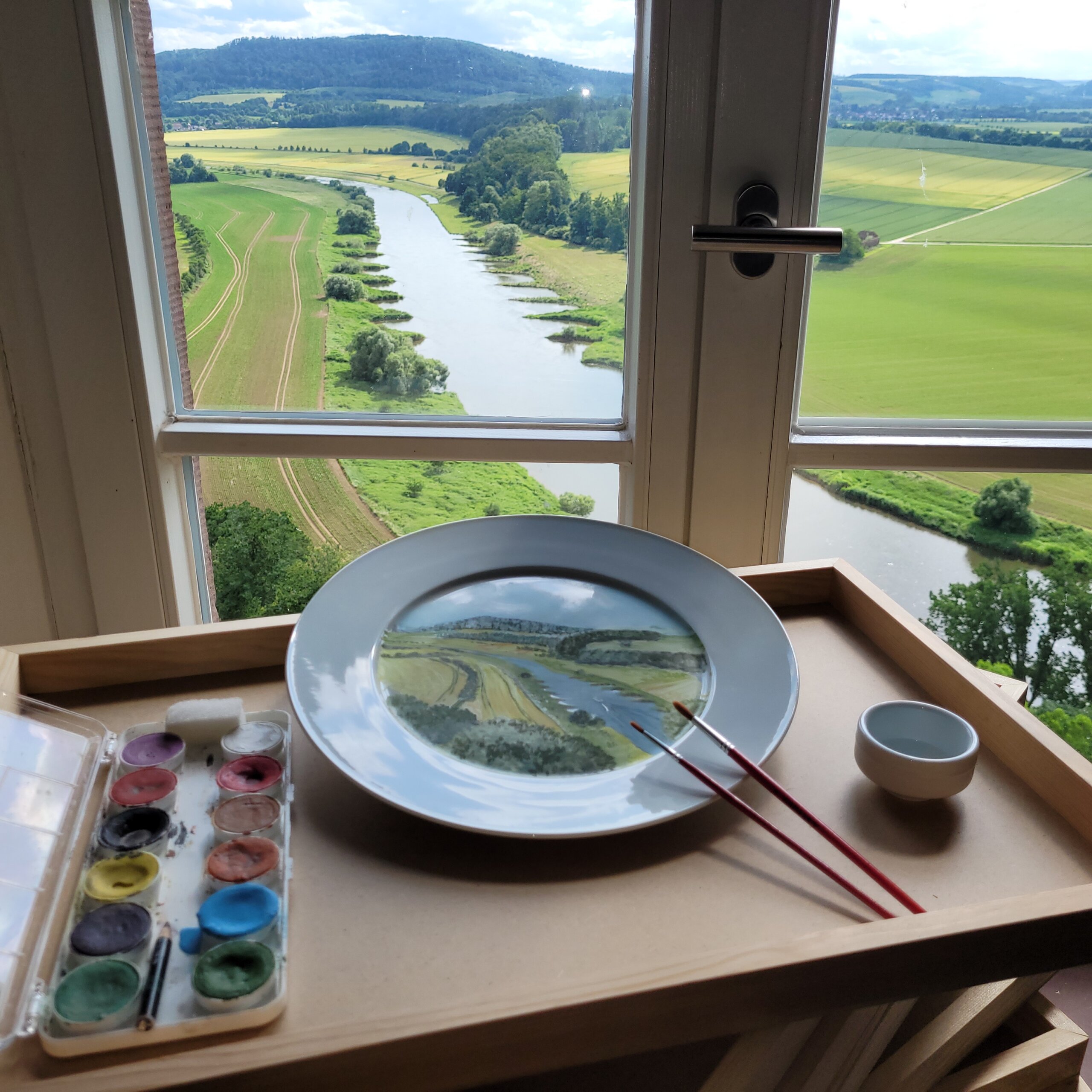 Porzellenteller und Porzellanmalfarben stehen vor dem Fenster